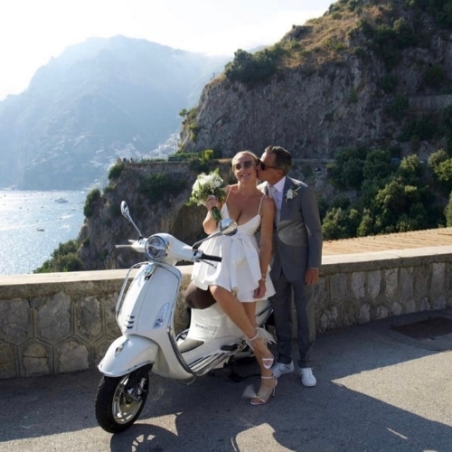 Bruidspaar bij een Vespa aan de Amalfikust met bergen en zee op de achtergrond.