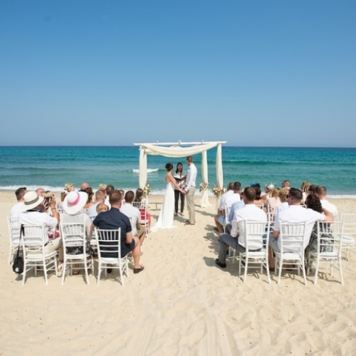 Trouwceremonie op het strand van Sardinië met gasten en uitzicht op zee.