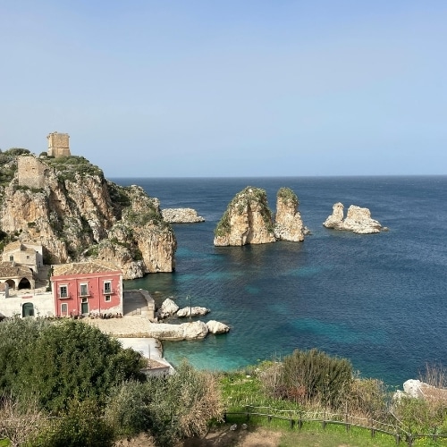 Kust van Sicilië met rotsen, helderblauwe zee en een kustdorp.