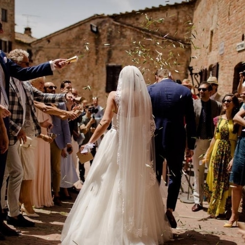 Bruidspaar loopt tussen de gasten door nadat ze voor de wet zijn getrouwd in een romantisch dorpje Toscane.