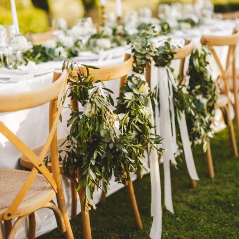 Stoelen met groene decoratie en linten aan een gedekte tafel voor een buitenbruiloft in Italië.