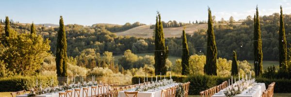 Gedekte tafels voor een buitenbruiloft in Toscane, met cipressen en heuvels op de achtergrond.